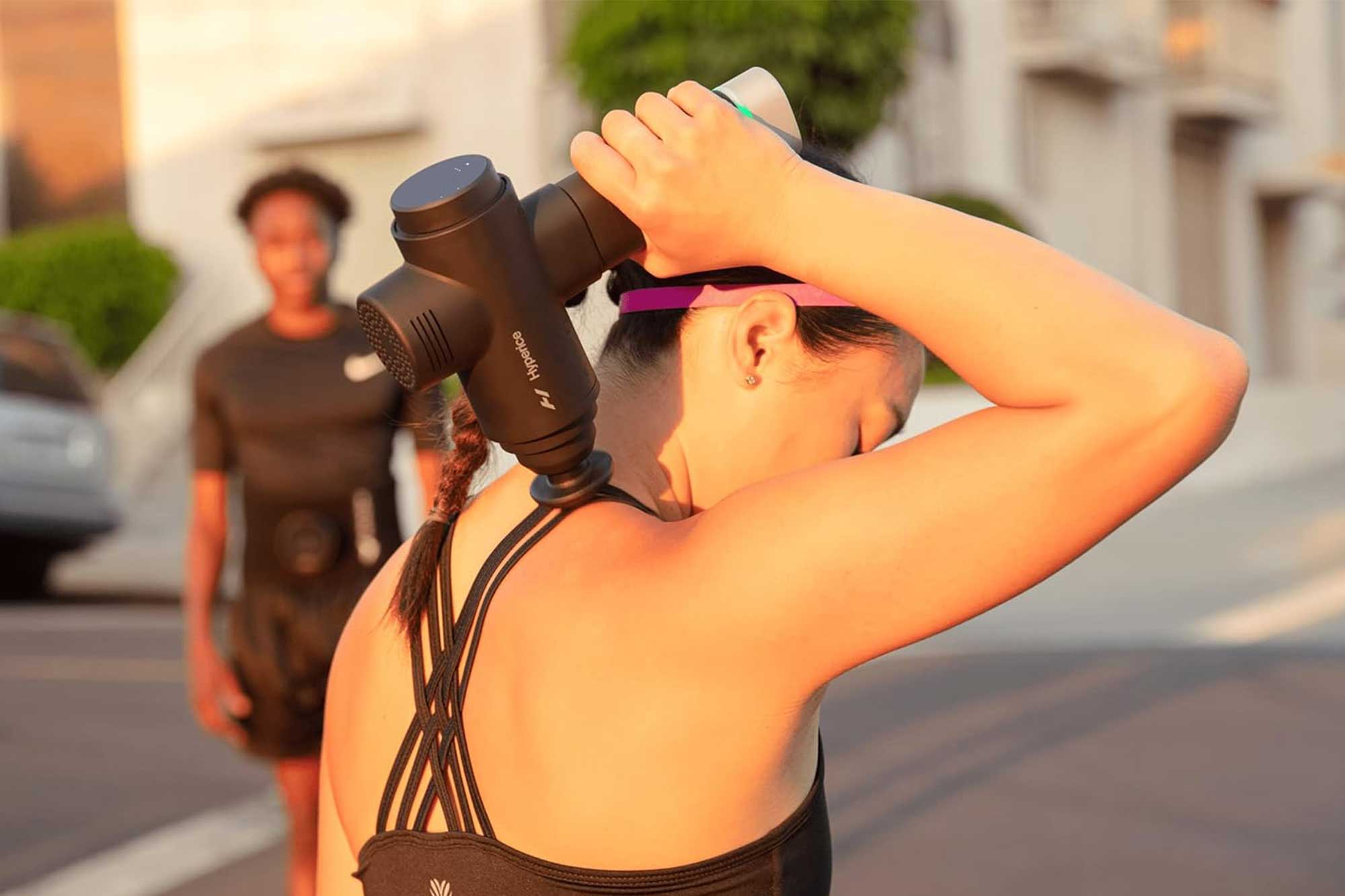 A person using a Hyperice Volt 2 percussion massager on their shoulders