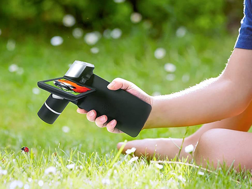 A person holding a mini portable microscope and using it to look at grass