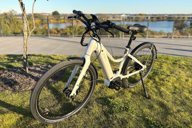 The Priority Current Plus electric commuter bike in white parked on the grass overlooking the Potomac River and DCA airport in the background