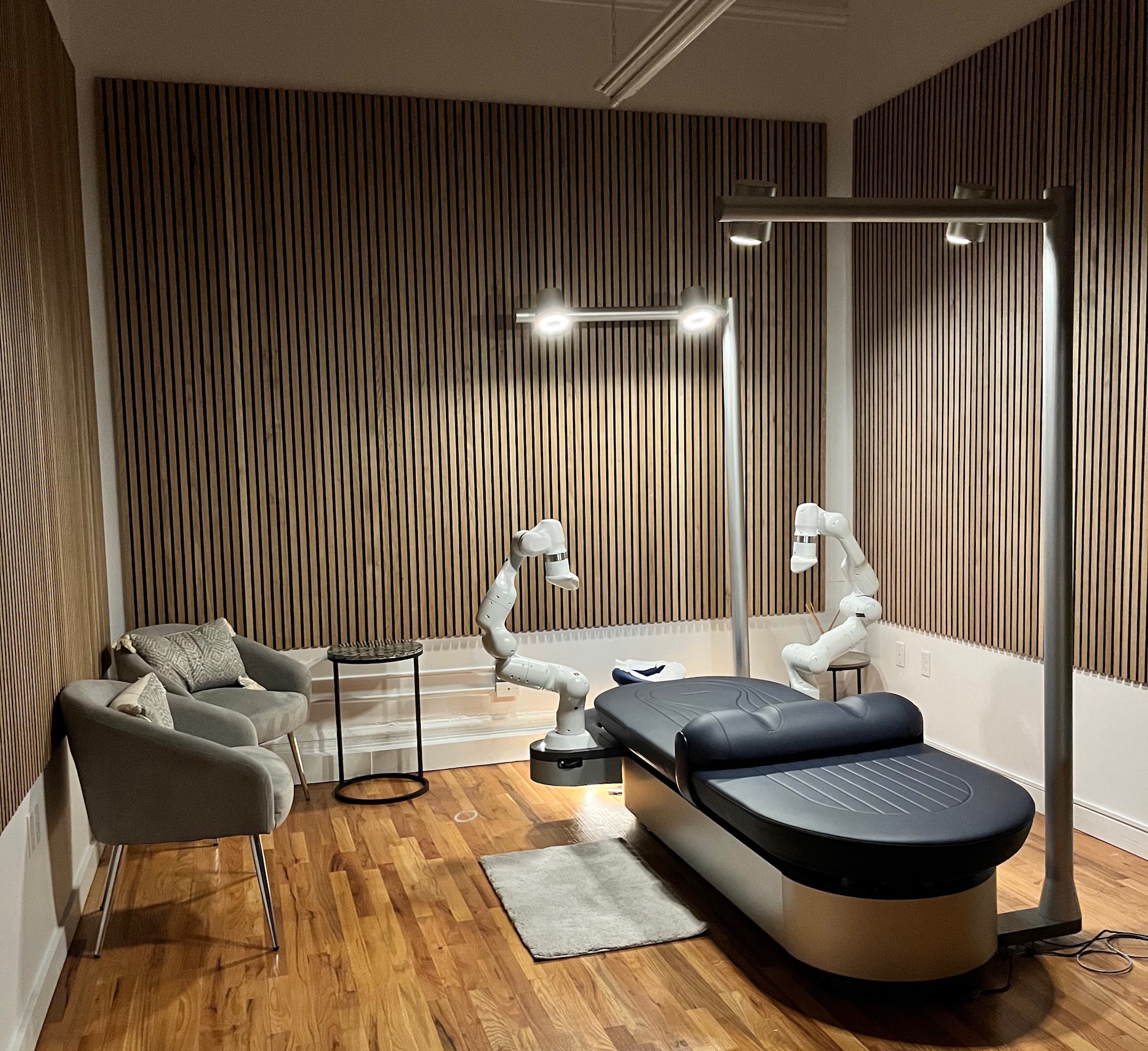 room with two chairs, wood on walls, massage table with robot arms