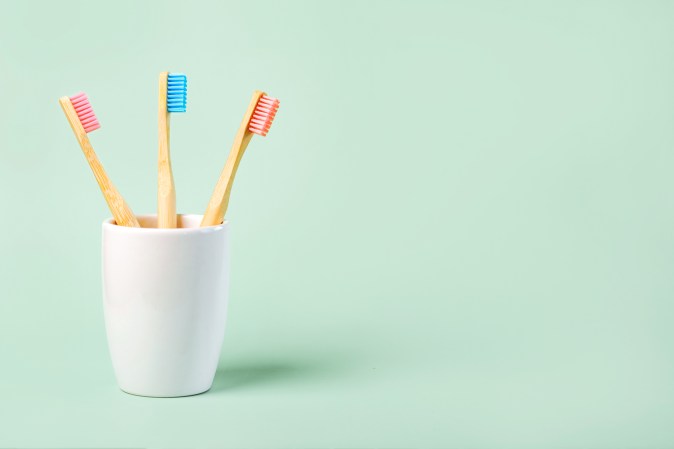 three colored bamboo toothbrushes in a ceramic glass on green background