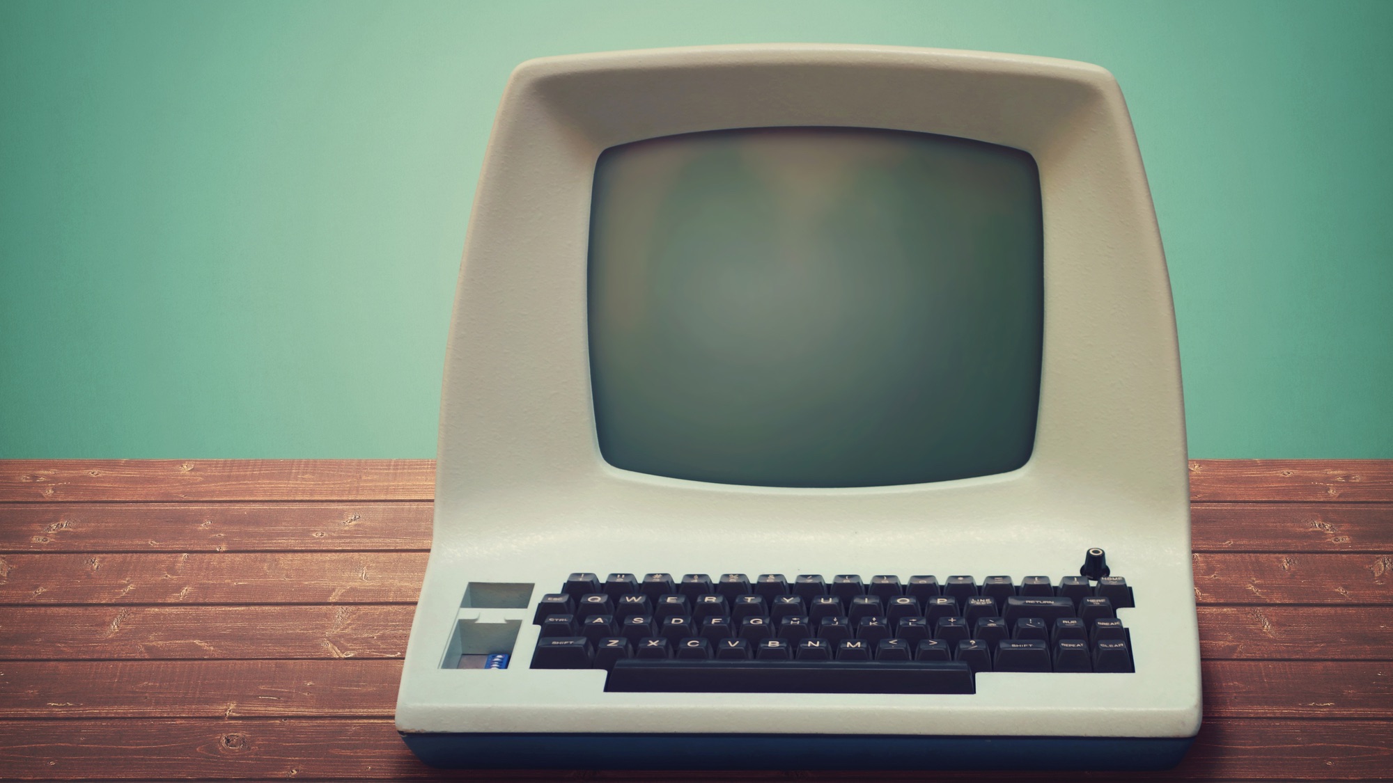 old-style computer on a wooden table with green wall