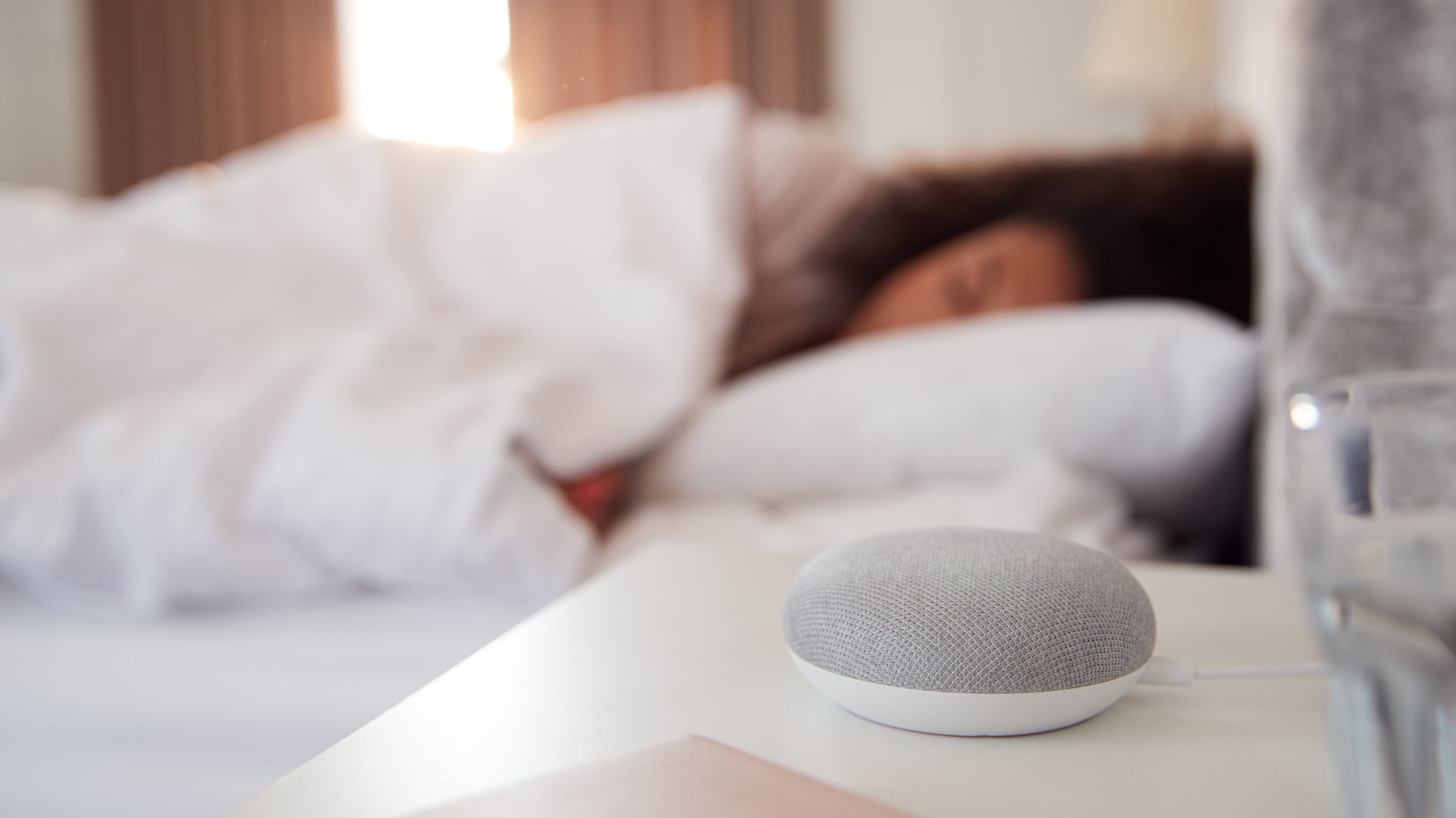 Woman Sleeping In Bed With Voice Assistant On Bedside Table Next To Her