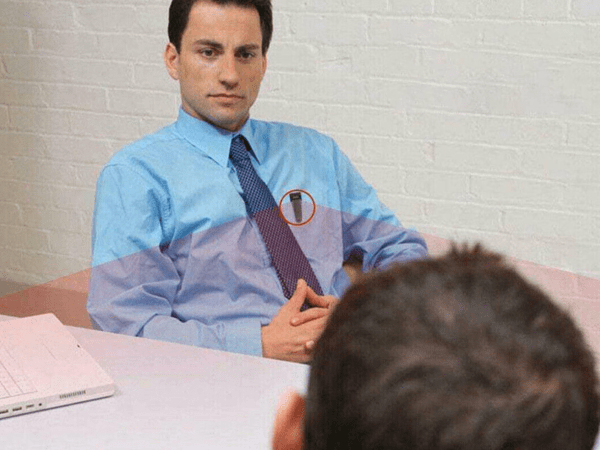 A person sitting across from another person at a table while wearing a body camera.