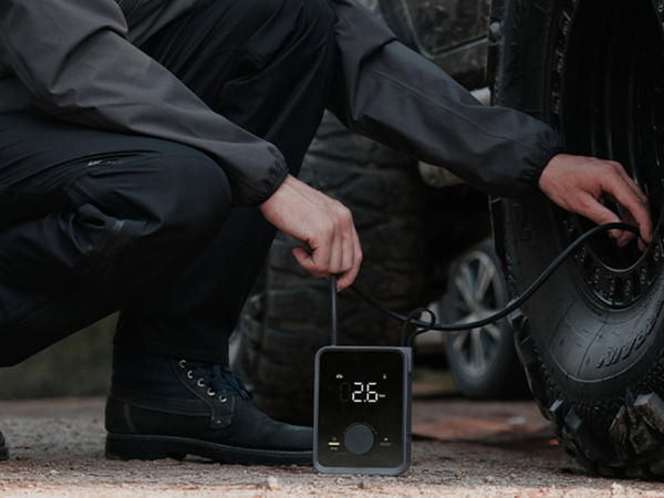 A person using a portable, compact inflator to refill their tires