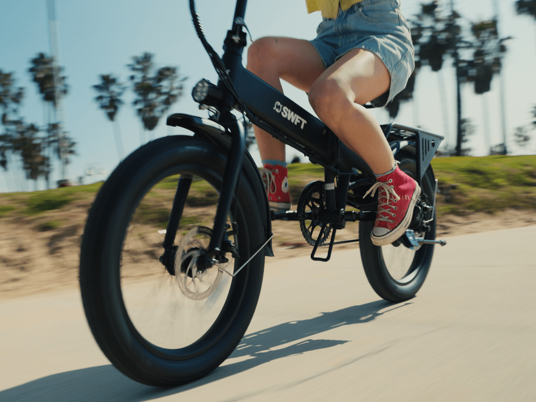 A person riding down a beachy sidewalk on a folding e-bike.