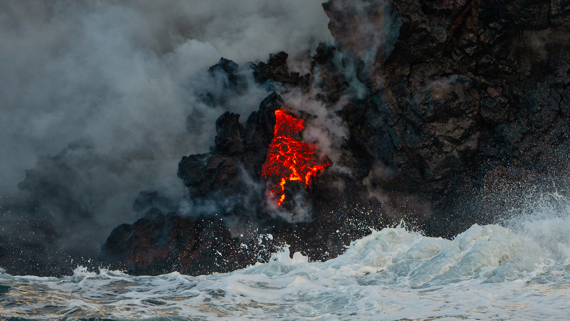 red lava rushes into the Pacific Ocean, with smoke and steam rising