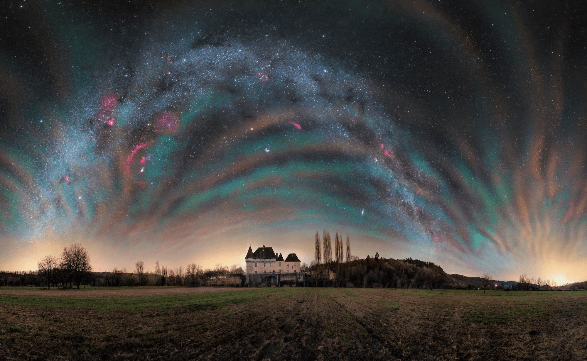 ripples of color and dots of stars above a large house on farmland