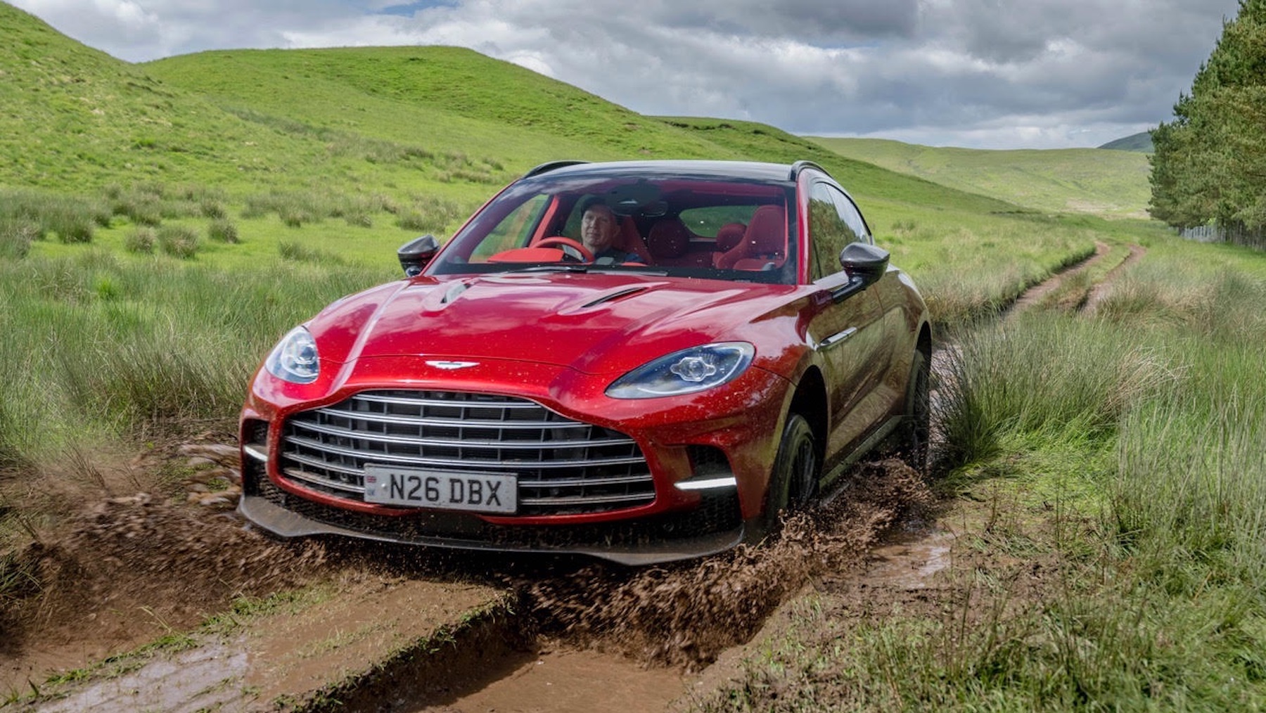 a red sports car splashy through mud next to green hills