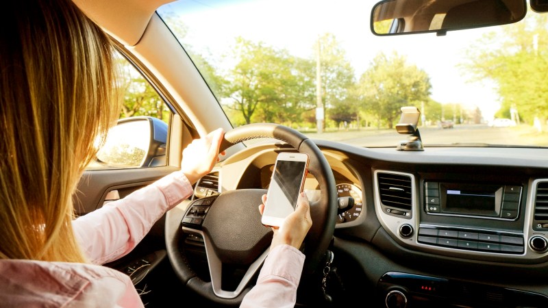Young woman holding blank screen cell phone, driving car.