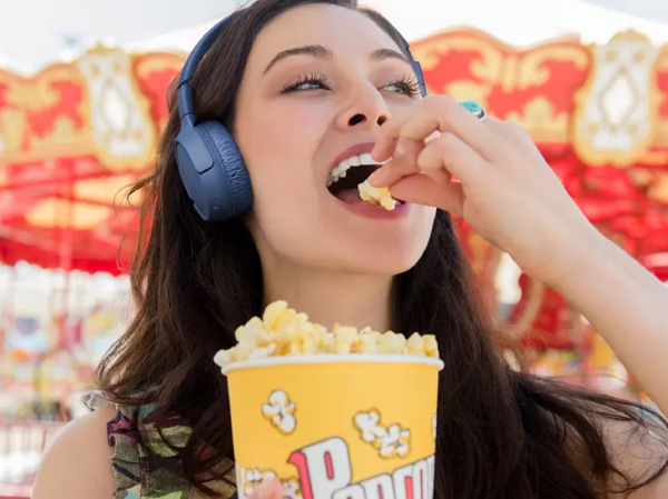 A woman eating popcorn while wearing a pair of JBL Tune 510BT Wireless On-Ear headphones