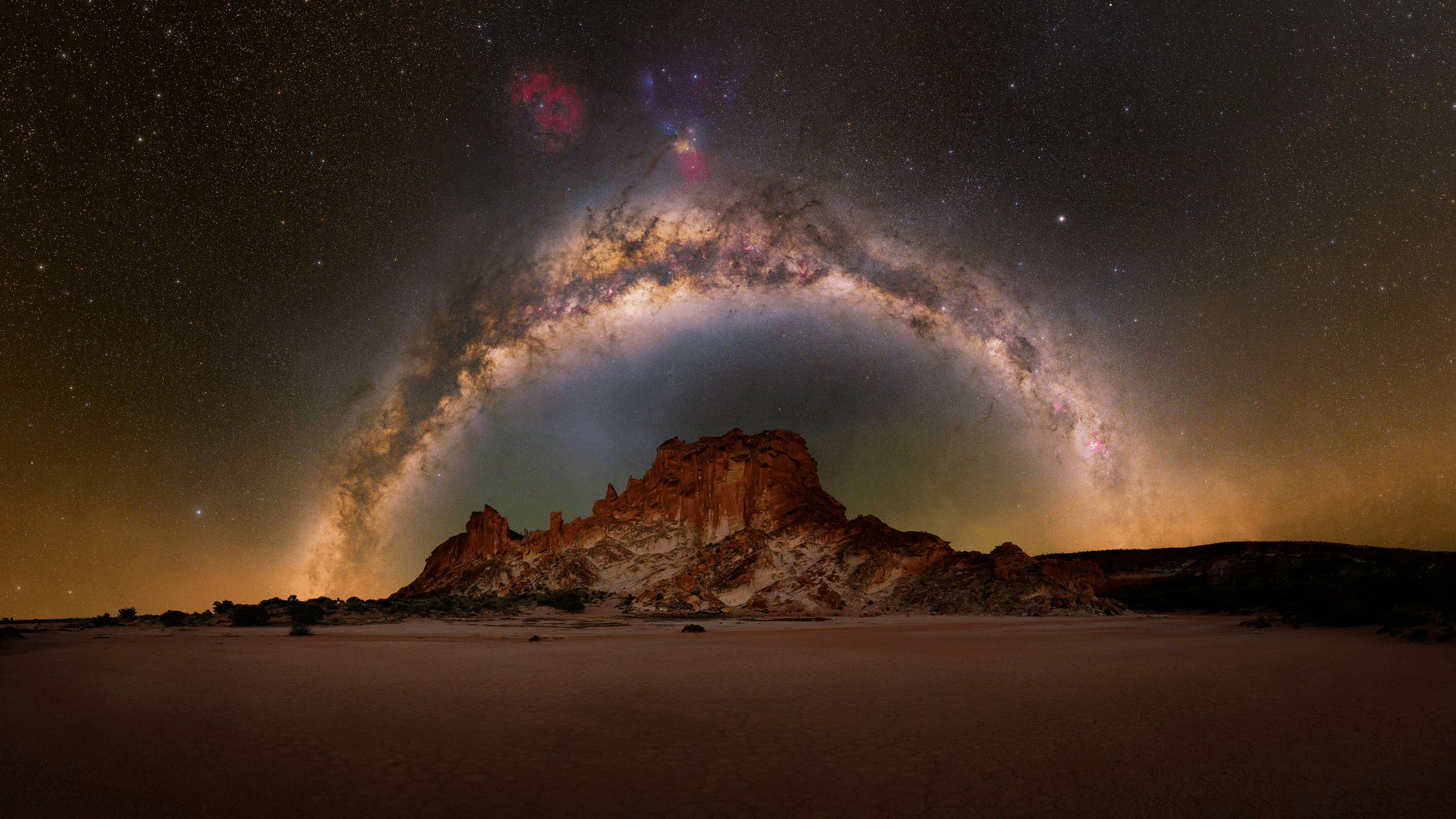 an outcrop of sandstone in the flat desert with a half circle of the milky way above