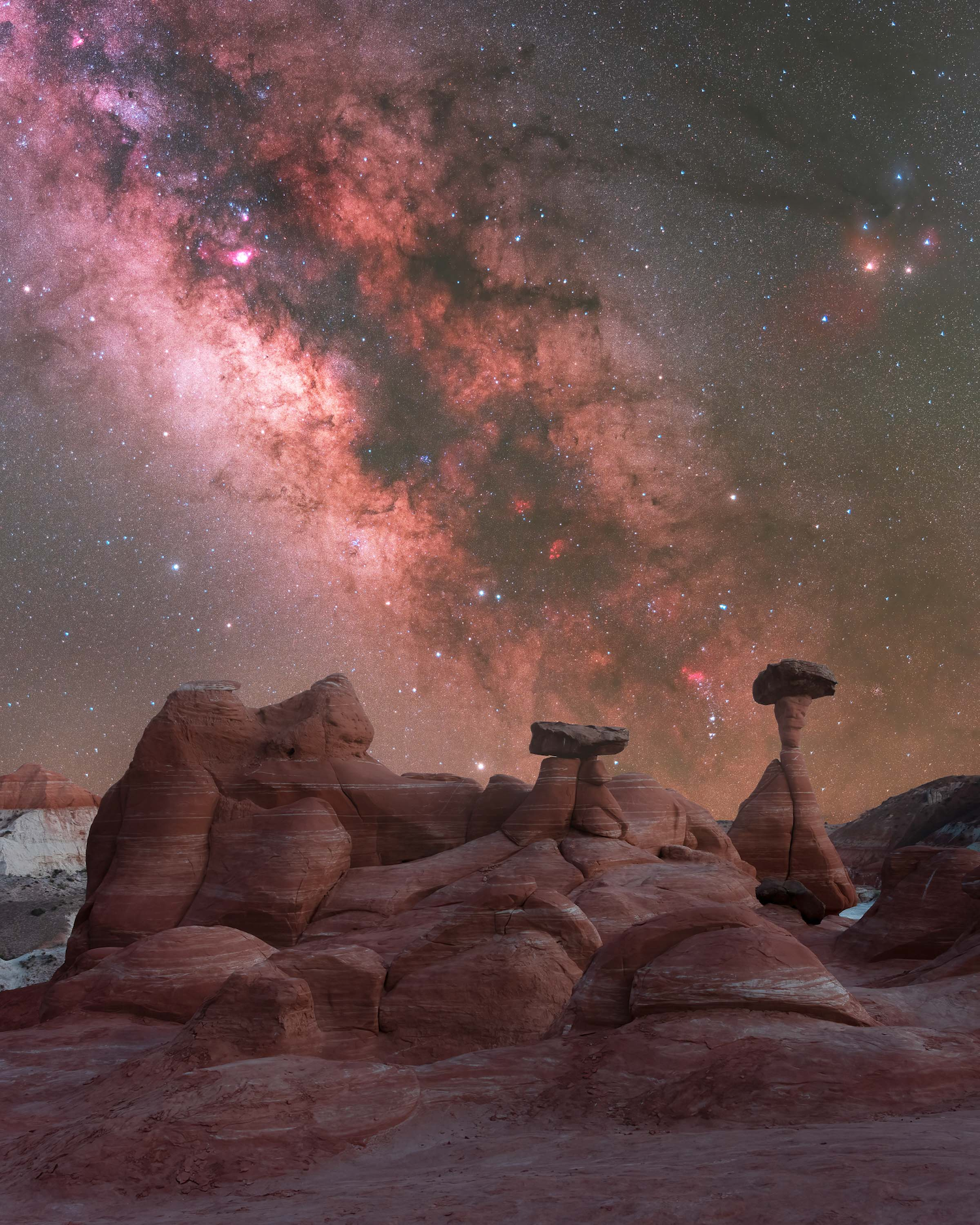 desert rock formations under stars and a reddish cloud of space dust