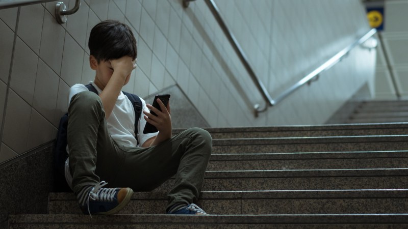Sad child in stairwell using phone