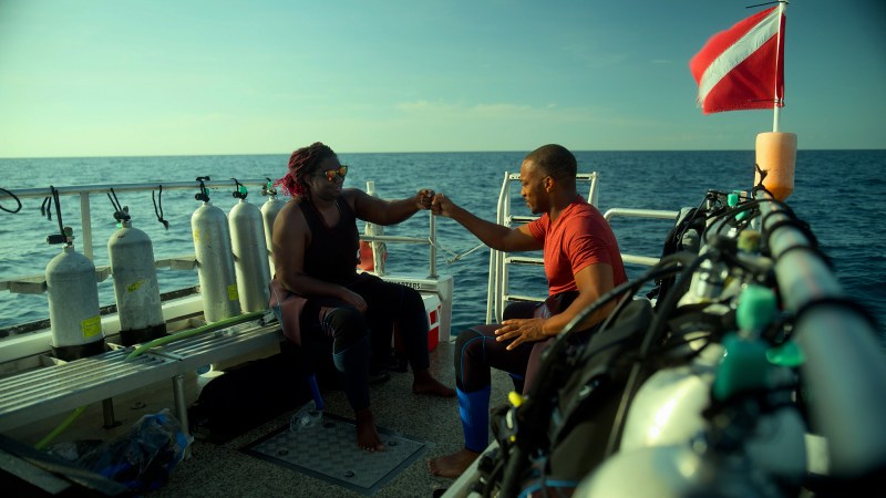 a marine biologist and an actor fist bump while sitting on a dive boat in the ocean