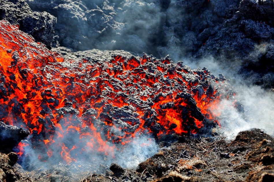 a close up of orange and black lava, with white smoke billowing.