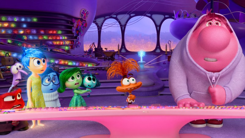 still from the animated film "inside out 2." red anger, purple fear, yellow joy, blue sadness, and green disgust meet with new emotions. Envy is teal, anxiety is orange, and embarrassment is pink.