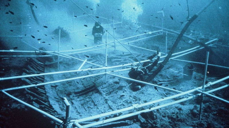 the wreckage of an ancient greek shipwreck underwater, with two divers exploring it