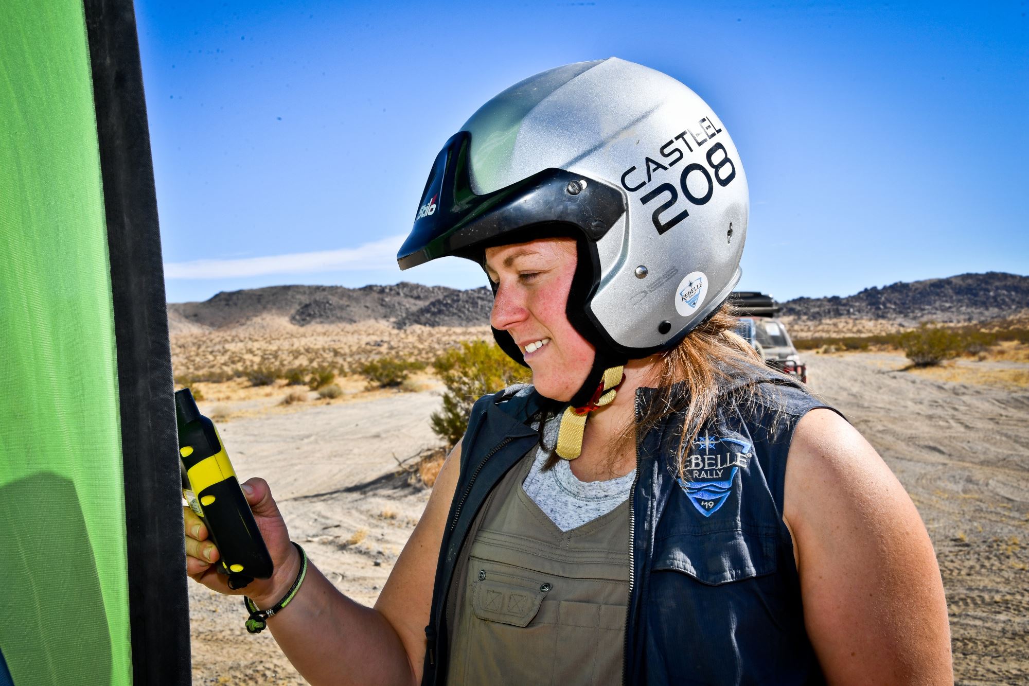 woman in a helmet using a tool in the desert in front of SUV