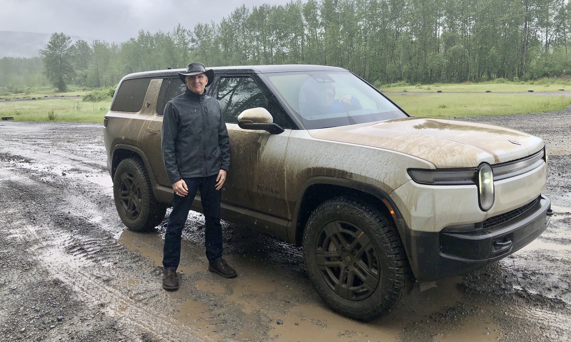 man stands in front of muddy suv on rainy day