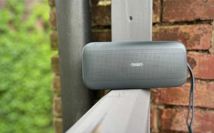  A gray Tribit StormBox Flow portable speaker on a wooden railing outdoors.