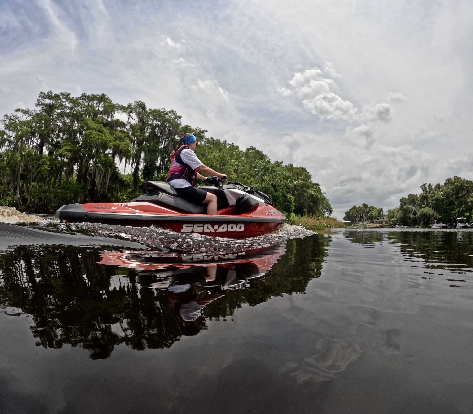 a woman rides a watercraft vehicle on a river with trees on the bank