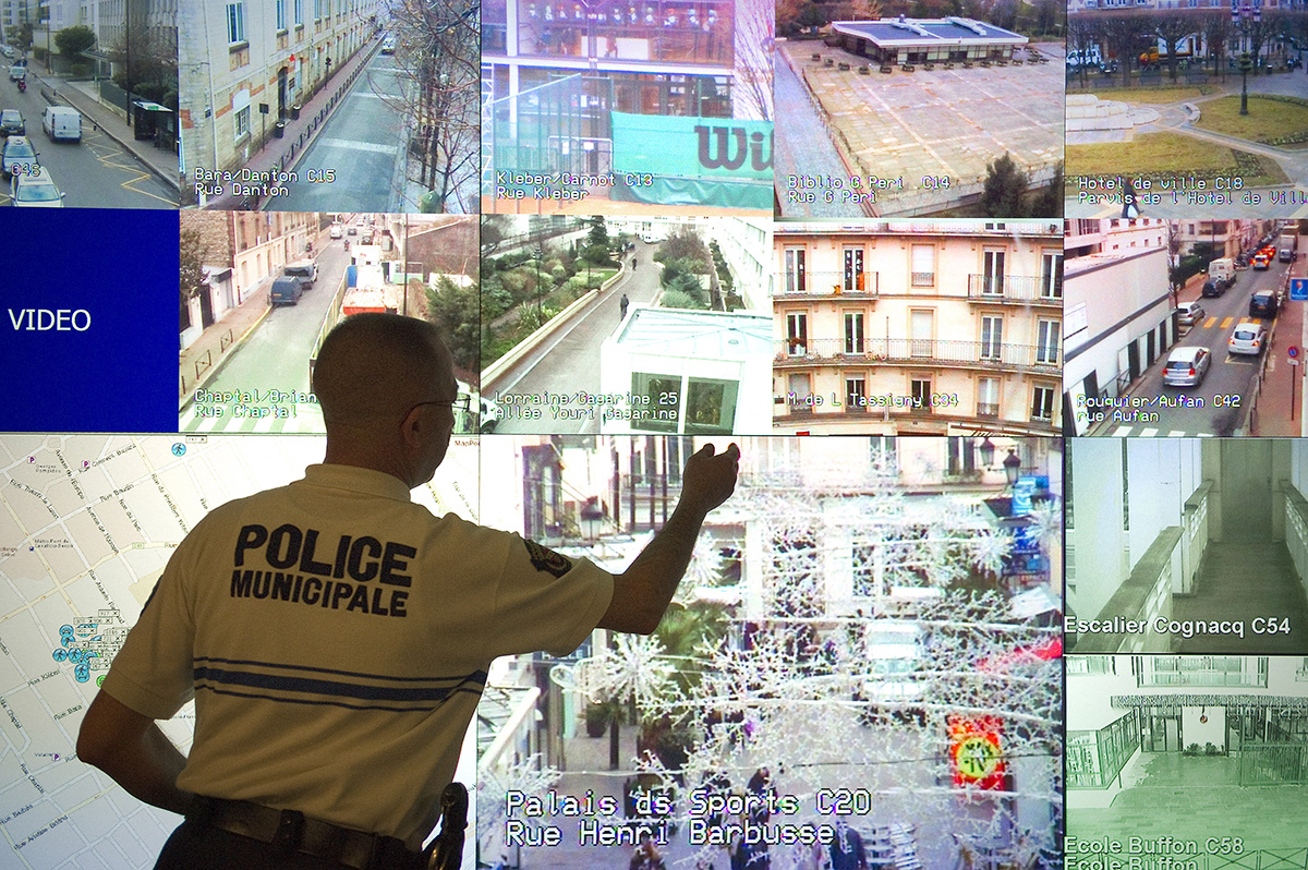 A policeman stands in front of a giant screen featuring videos taken from surveillance cameras in the streets of Levallois-Perret, outside Paris on January 10, 2012 at Levallois police station. AFP PHOTO LIONEL BONAVENTURE (Photo by LIONEL BONAVENTURE / AFP) (Photo by LIONEL BONAVENTURE/AFP via Getty Images)