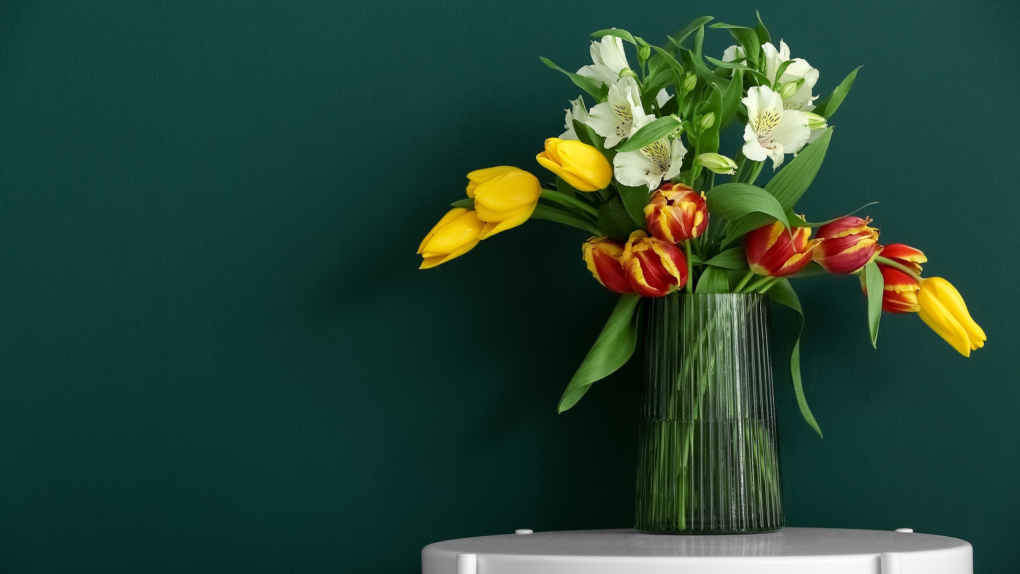 Vase with flowers on table near color wall