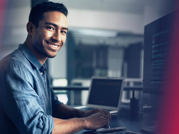 A person looking at a camera while coding and smiling.