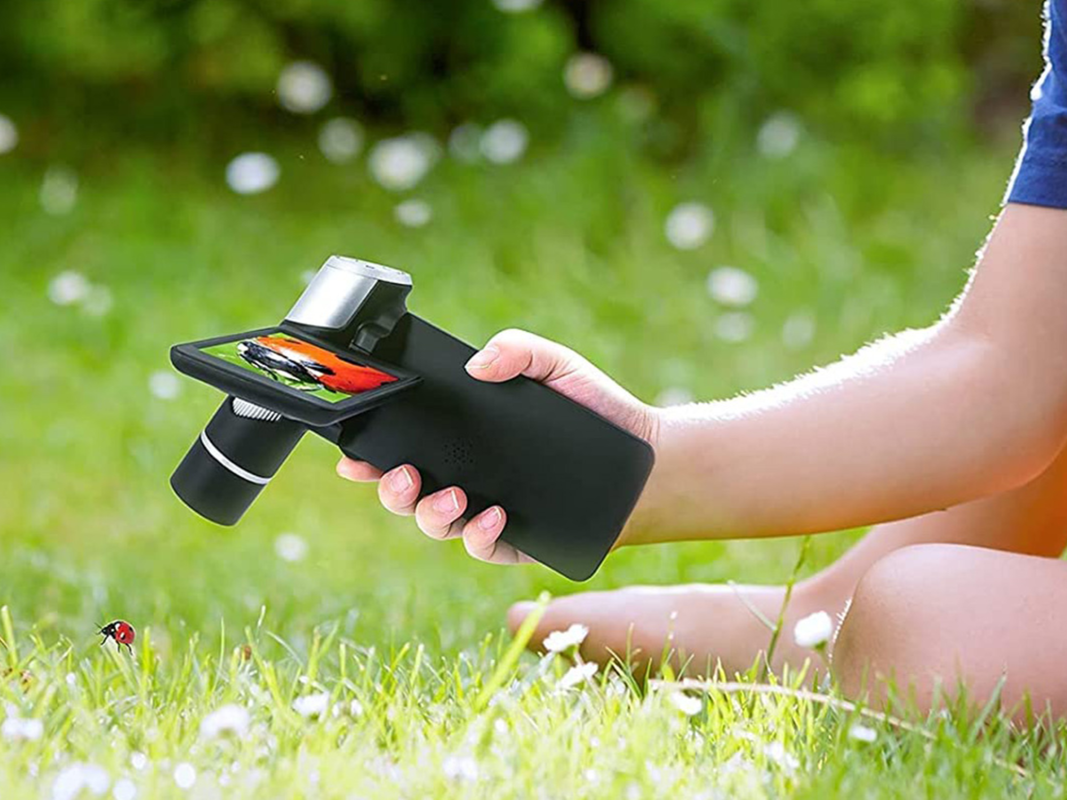 A person looking at grass through a portable microscope.