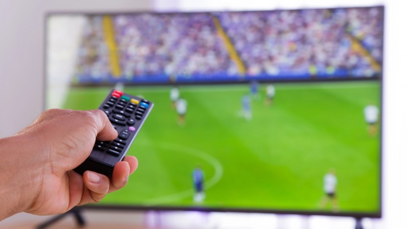 a hand holding a remote in front of a TV playing a soccer match
