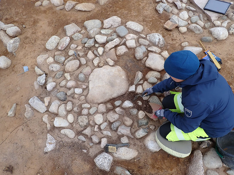 an archeologist digs near several grey and white stones placed in a circle