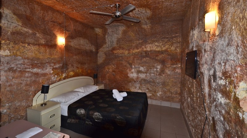 a hotel room that is entirely rock walls. a bed is pictured in the center