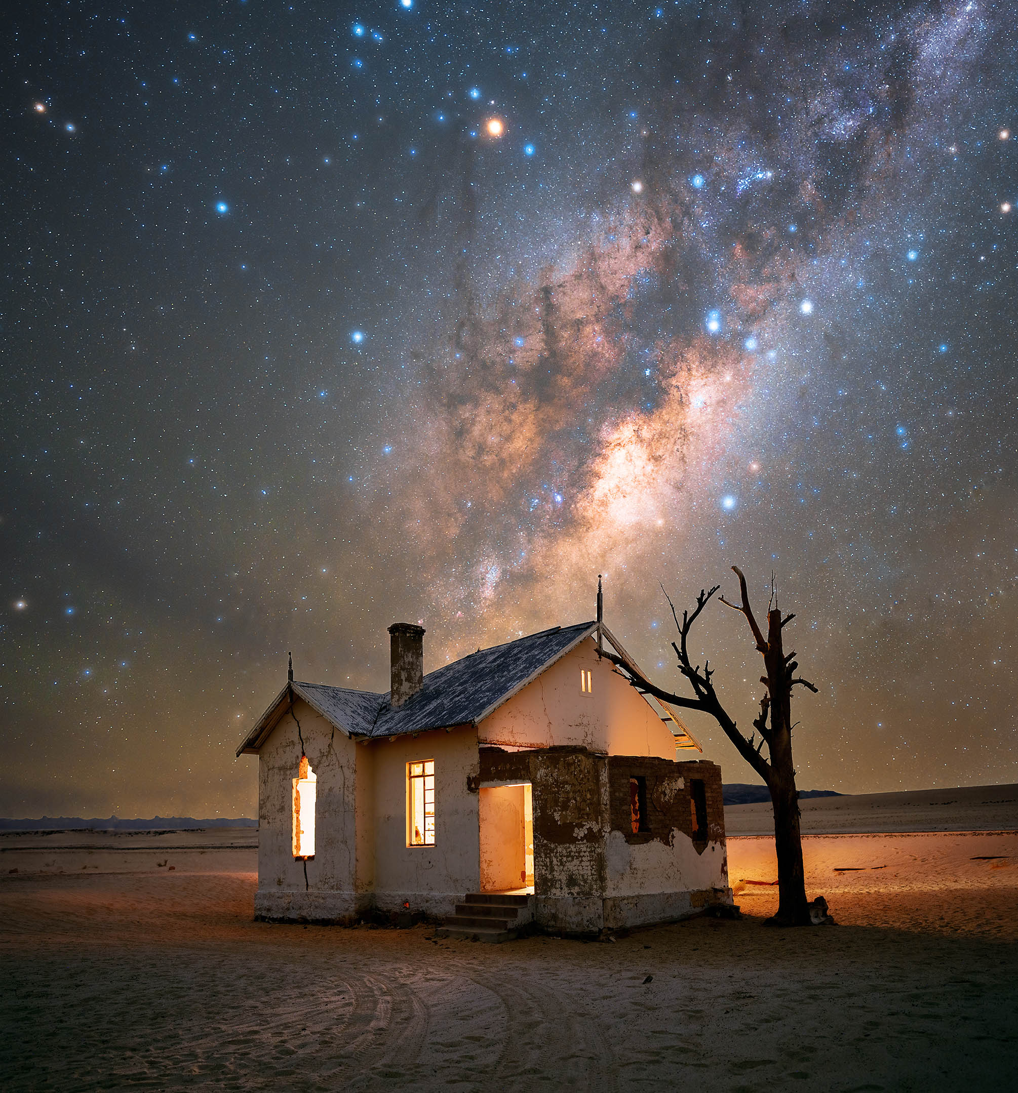 the milky way and thousands of stars above an abandoned house and dead tree