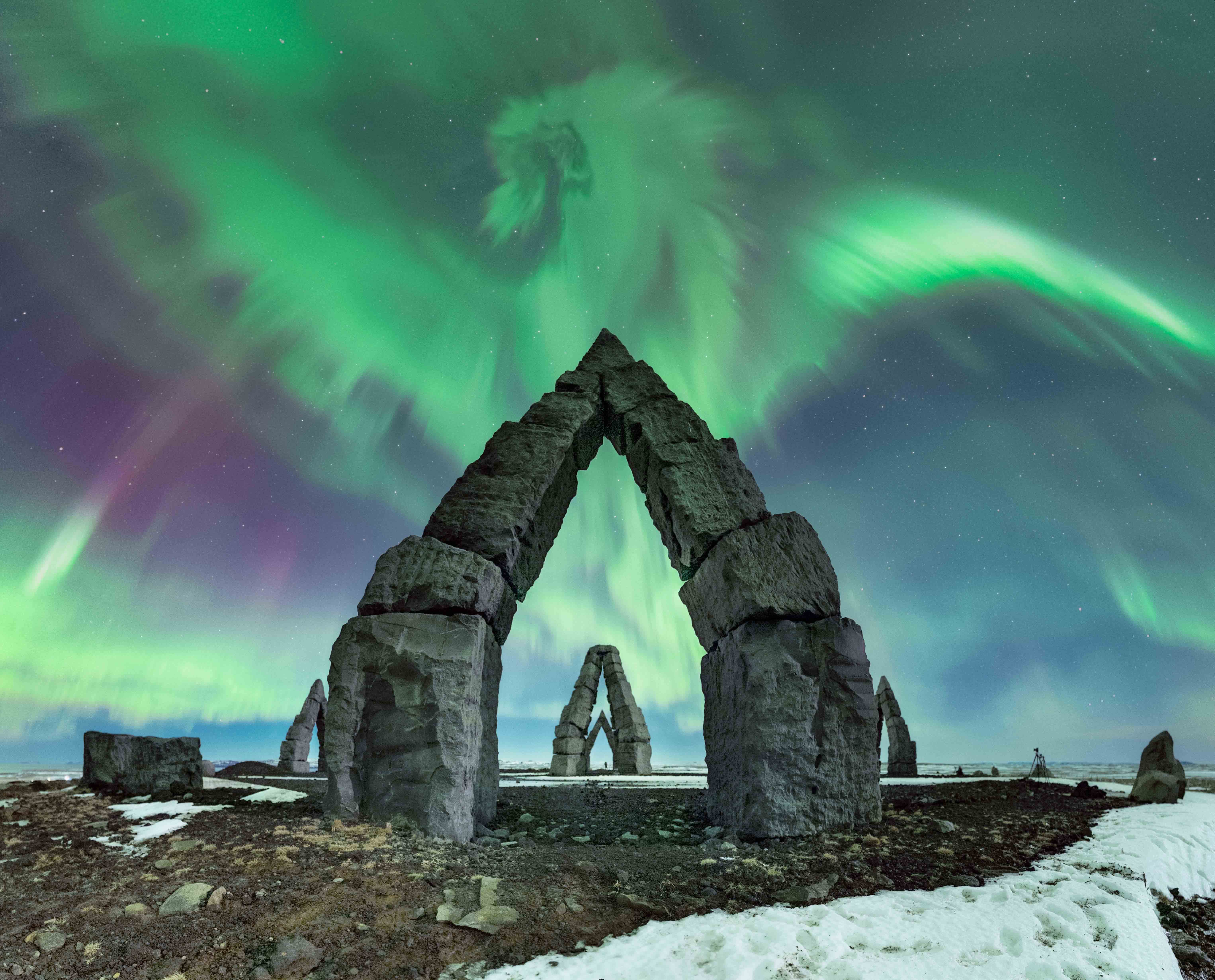 a green and purple aurora above rock structures shaped like upside-down Vs