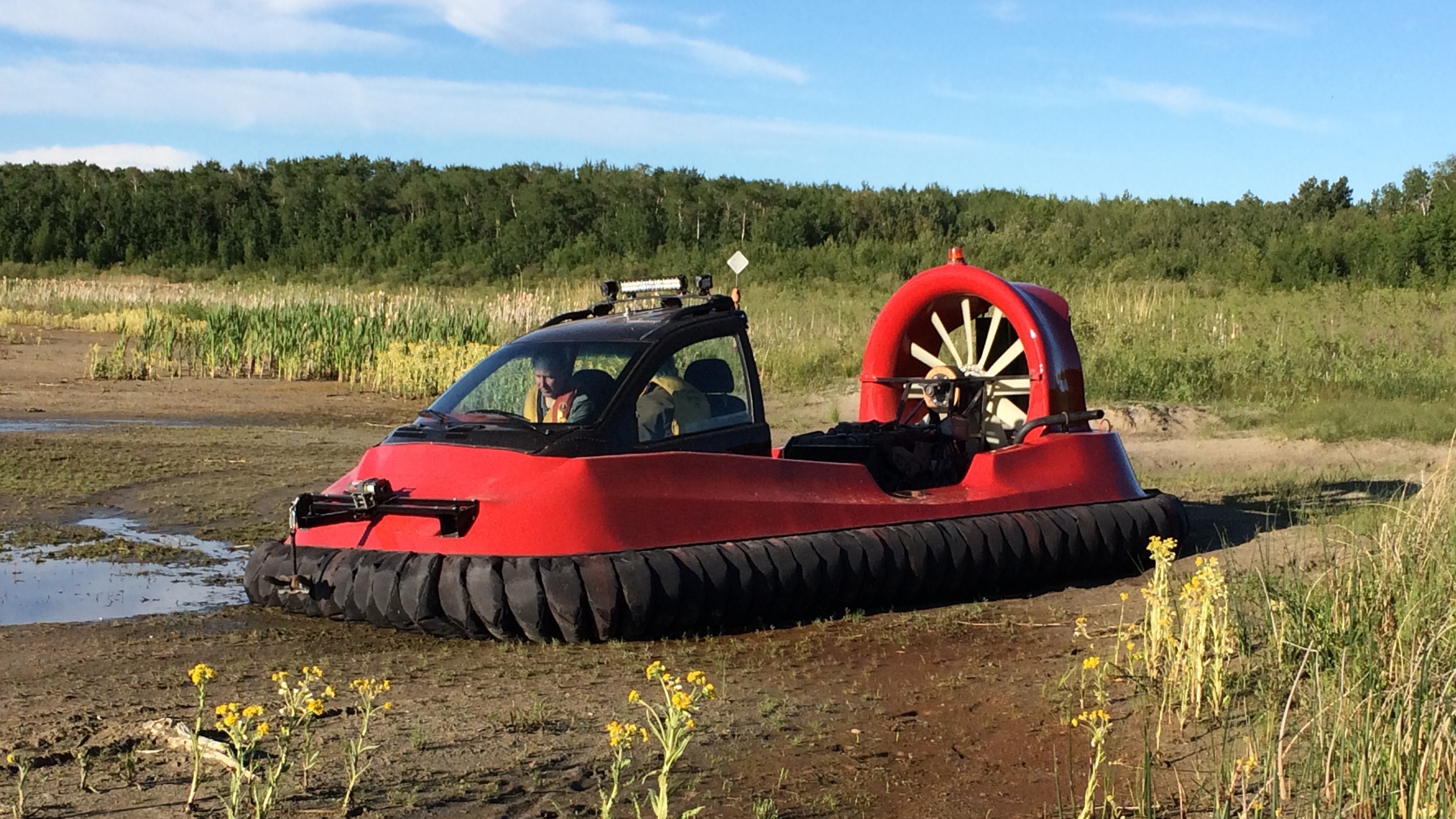 a red hovercraft vehicle sits on the mud with two occupants in the cabin