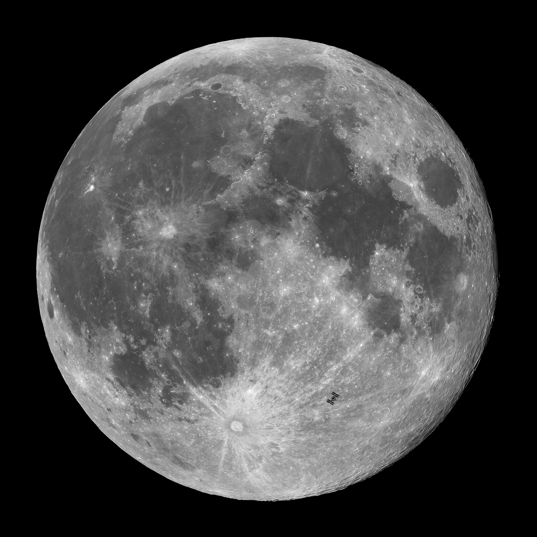 The International Space Station appears tiny against the full moon