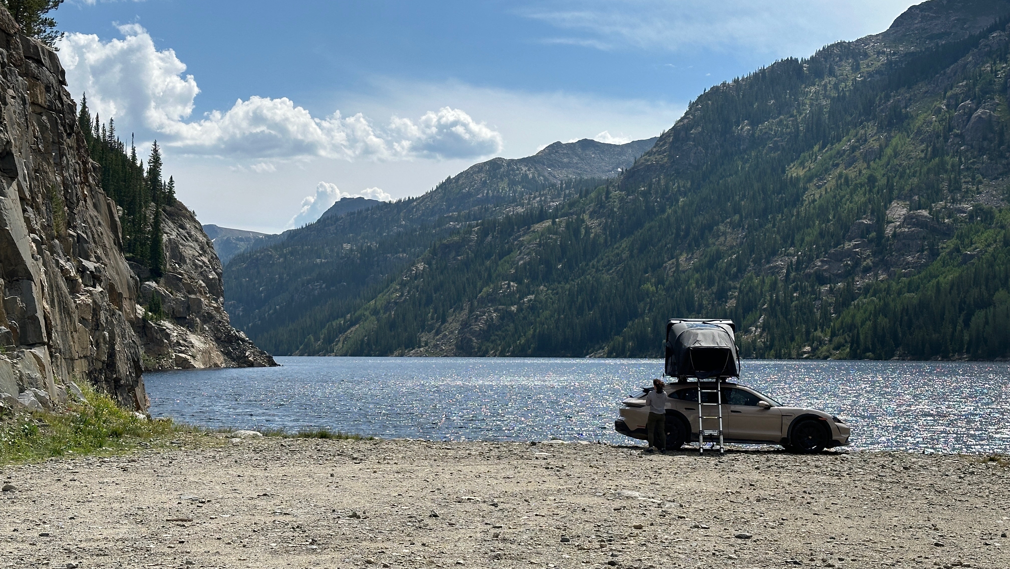 an SUV with a pop tent on top and a ladder in front of a mountain lake