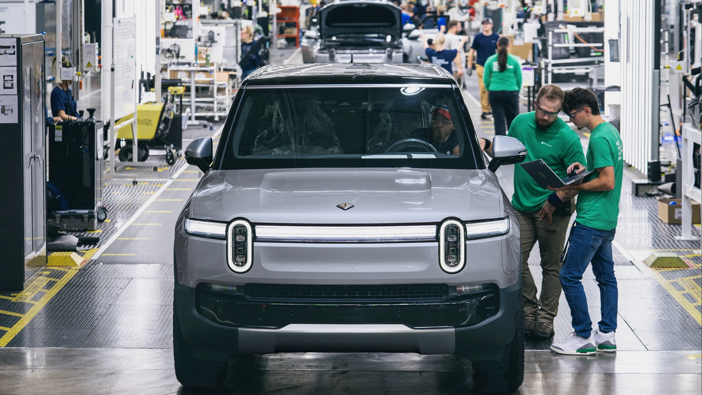 an SUV rolls down an assembly line with people inspecting it