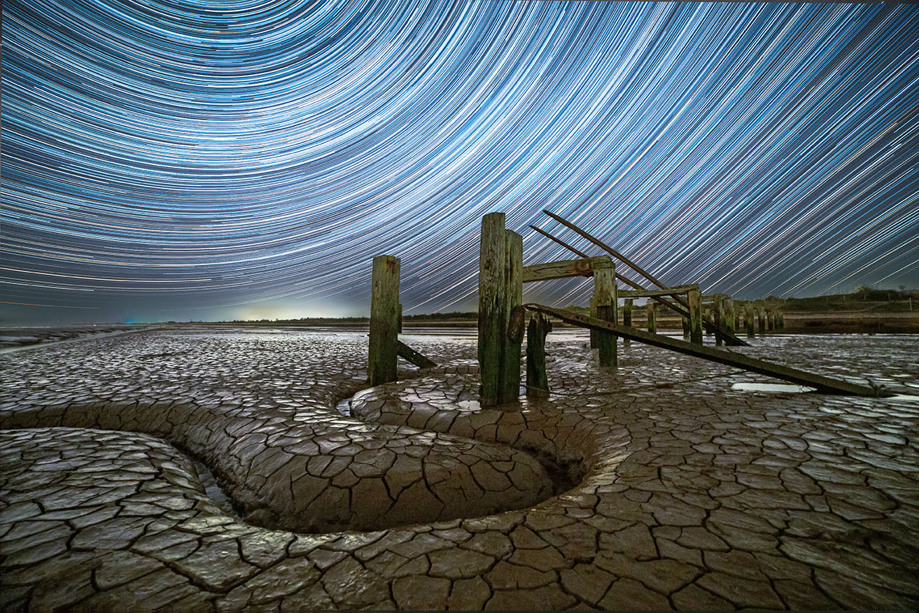 Time-lapse-fotografie van sterren die door de hemel bewegen, weergegeven als strepen met een gebarsten woestijn op de voorgrond 