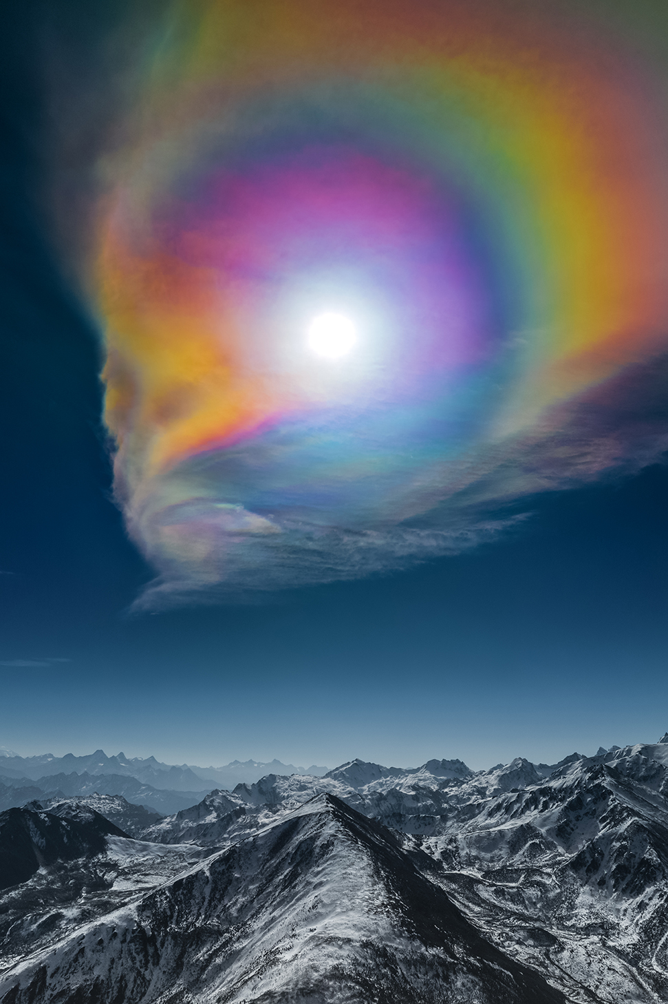 a rainbow of color appears around the sun above mountains 