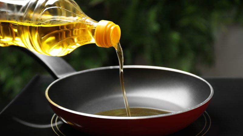 Pouring cooking oil from bottle into frying pan, closeup