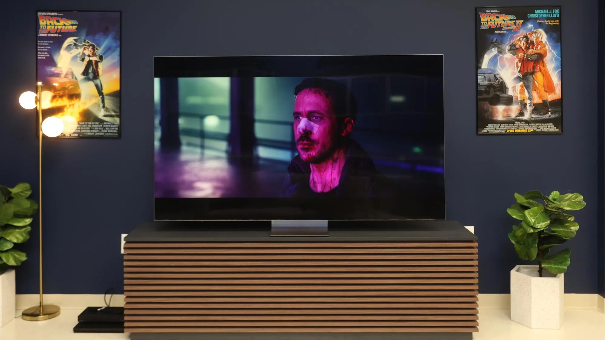 a TV with actor ryan gosling on it. the setting is a living room with back to the future posters on the wall