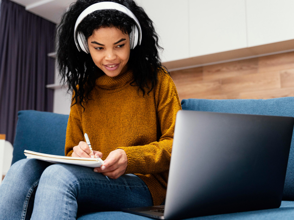 A person wearing headphones and taking notes off of a computer.