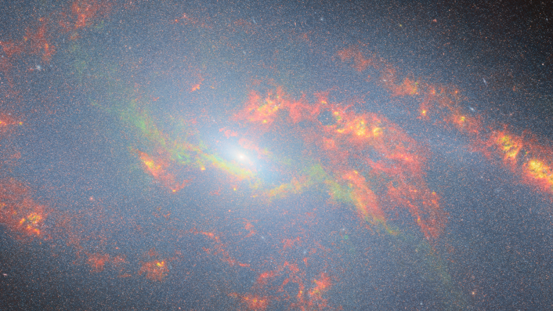 The central region of a spiral galaxy. Its core is a small bright point radiating bright, bluish-white light over the scene. The white light is diffuse and many point-like stars in the galaxy (and even background galaxies) can be seen through it. The galaxy’s arms can be seen as broad, swirling streaks of glowing gas and dust, coloured red and orange. Two additional arms are revealed in green