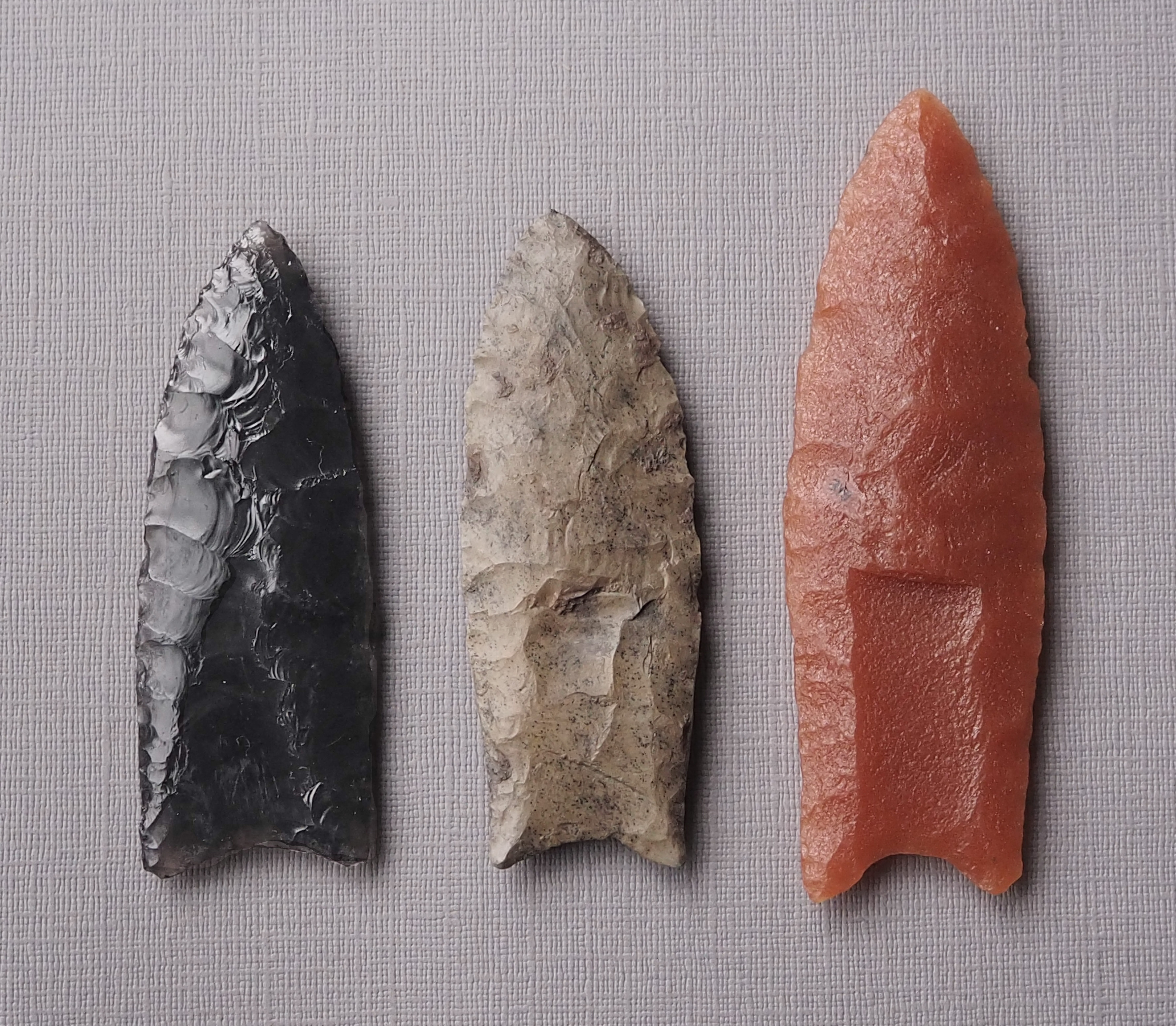 three clovis points. one is small and black, one is medium sized and white, the other is larger and orange