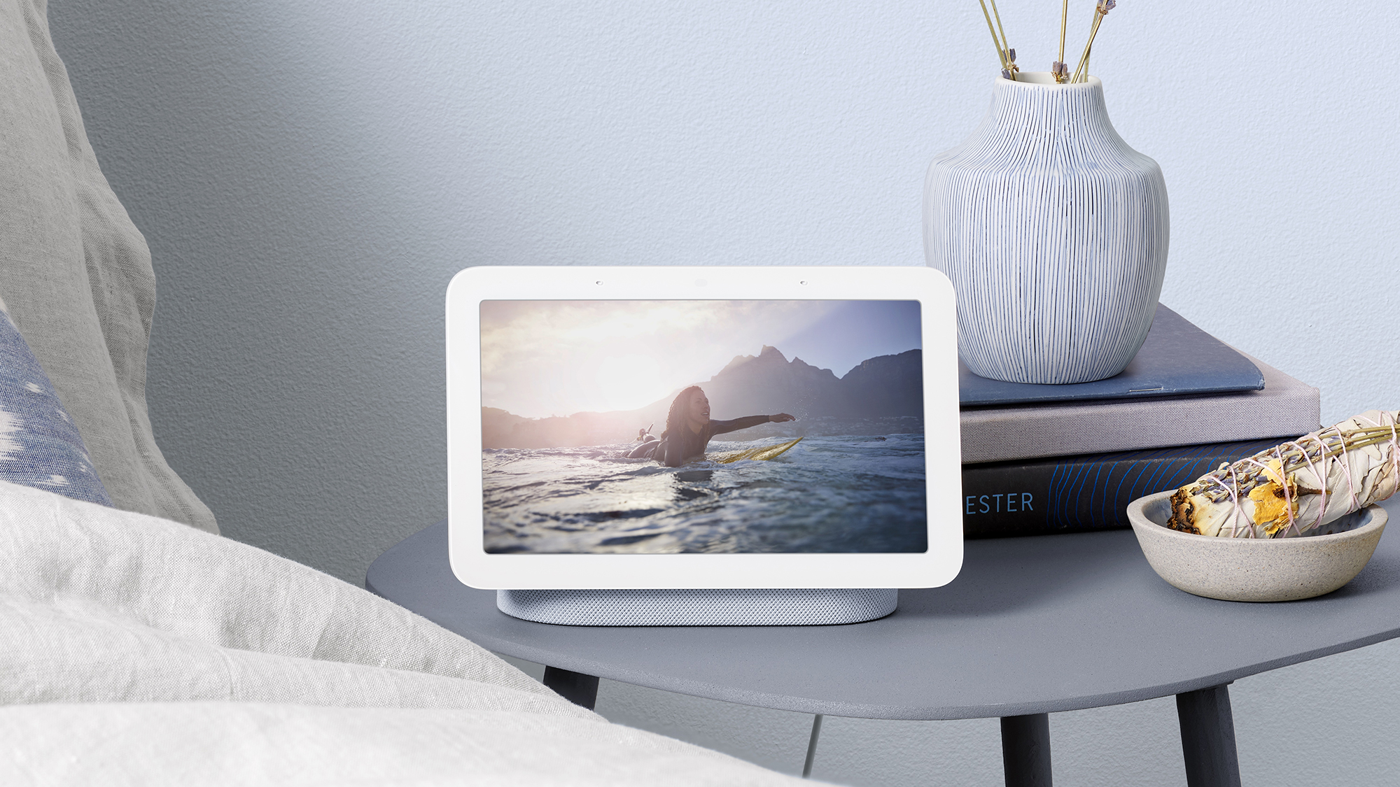 Google Home device on a nightstand in a bedroom with an image of a woman surfing the web displayed