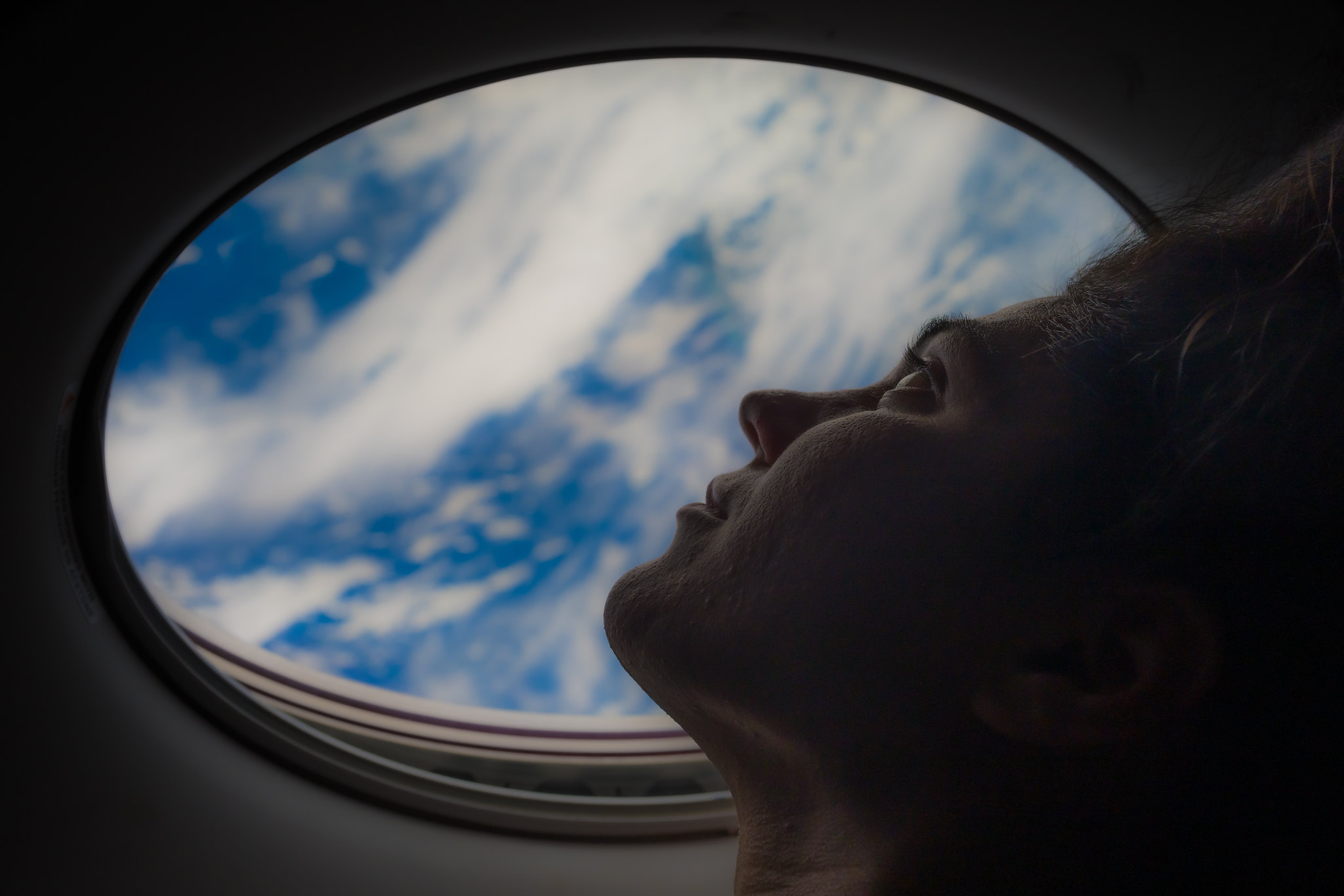 a woman looks out a window of space capsule, earth seen through window