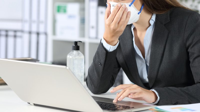 Woman working at desk with face mask on while sick