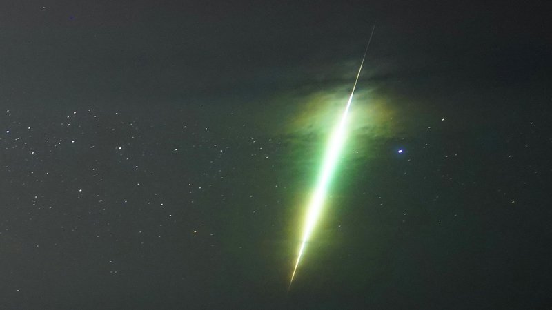 a bright green meteor streaks across the sky over cliffs